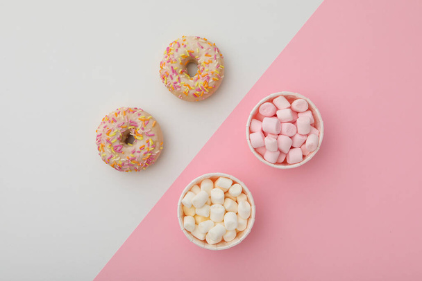 Donuts y malvaviscos en vasos de papel sobre fondo rosa y blanco, vista superior - Foto, imagen