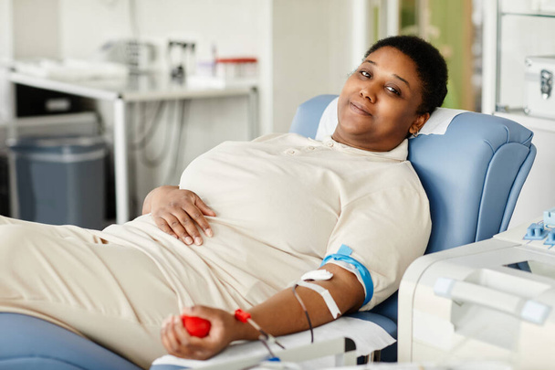 Portrait d'une femme souriante donnant du sang alors qu'elle était assise dans une chaise au centre de don de sang et regardant la caméra - Photo, image