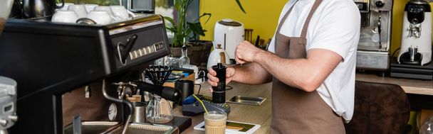Önlüklü barista, dijital tabletin yanında kahve öğütüyor ve kafede soğuk kahve içiyor. - Fotoğraf, Görsel