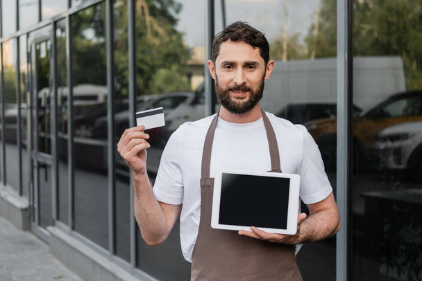sorridente barista segurando cartão de crédito e tablet digital com tela em branco na rua urbana - Foto, Imagem