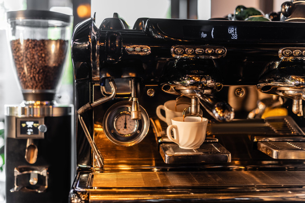 café derramando da máquina de café na xícara perto moedor borrado com luz solar no café - Foto, Imagem