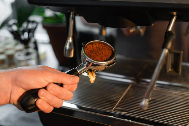 vista recortada del titular de la bodega barista con café cerca de la máquina de café borrosa en la cafetería - Foto, Imagen