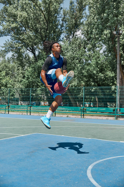 Slam dunk. Full-length image of young man in motion, playing basketball outdoors on sportsground on warm day. Concept of professional sport, competition, hobby, game, active lifestyle - Foto, imagen