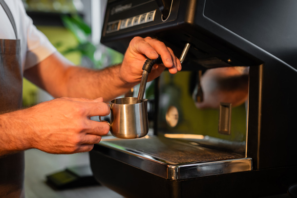 vágott kilátás barista habzó tej kancsóban a kávéfőző, miközben dolgozik a kávézóban - Fotó, kép