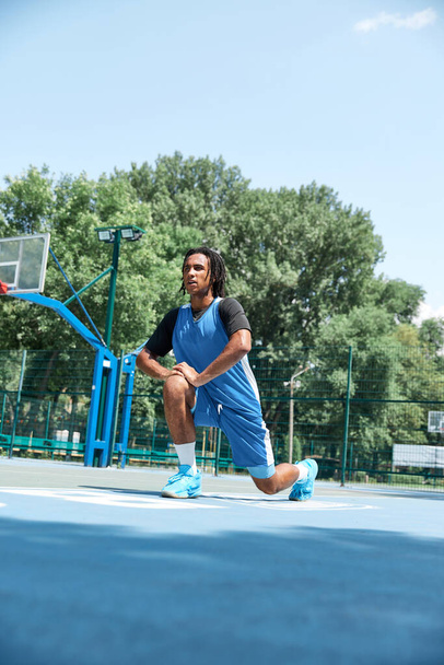 Young man, guy with dreads in uniform stretching before game, basketball training outdoors. Warm sunny day. Concept of professional sport, competition, hobby, game, active lifestyle - Photo, image