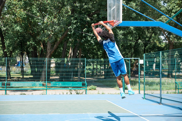 Dynamic image of young man, basketball player in motion, throwing ball into basket. Outdoors training. Concept of professional sport, competition, hobby, game, active lifestyle - Fotó, kép