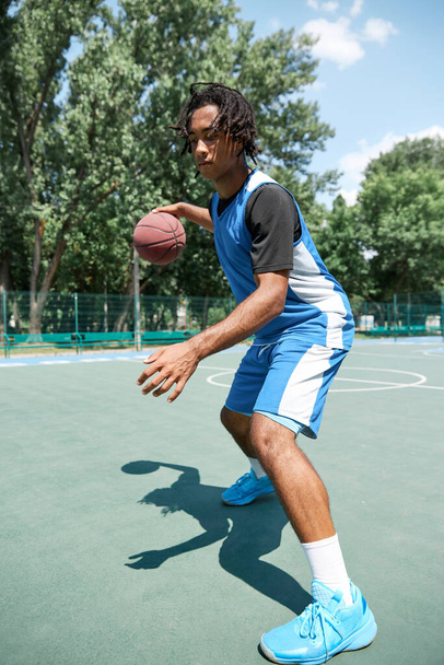 Young man, athlete in blue uniform training, playing basketball outdoors on warm summer day. Concept of professional sport, competition, hobby, game, active lifestyle - Fotoğraf, Görsel