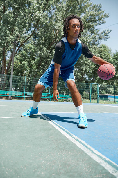 Ball dribbling. Young guy, basketball playing during game, training on outdoor sportsground on warm sunny day. Concept of professional sport, competition, hobby, game, active lifestyle - 写真・画像