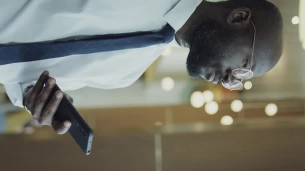 Vertical shot of African American businessman in formalwear typing on mobile phone - Felvétel, videó