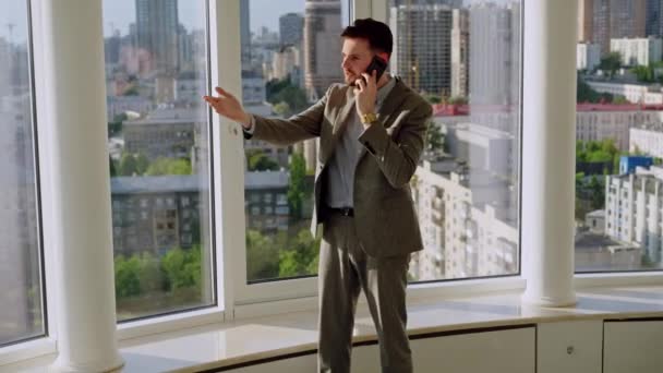 A successful young businessman in a nice suit in the office near the window picks up the phone and calls. The concept of happiness, success, and good emotions. High quality 4k footage - Materiał filmowy, wideo