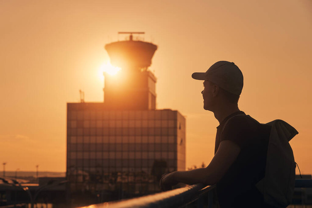 Traveler with backpack at airport. Silhouette of man against air traffic control tower at sunset - Φωτογραφία, εικόνα