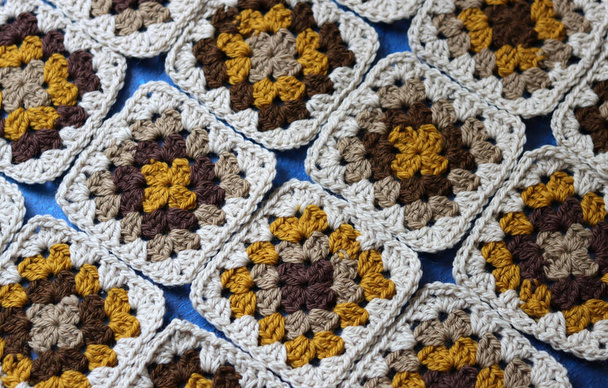 Crocheted granny squares made of natural brown, mustard and beige wool. Soft and fluffy crochet ornament on blue textured background.  - Photo, Image