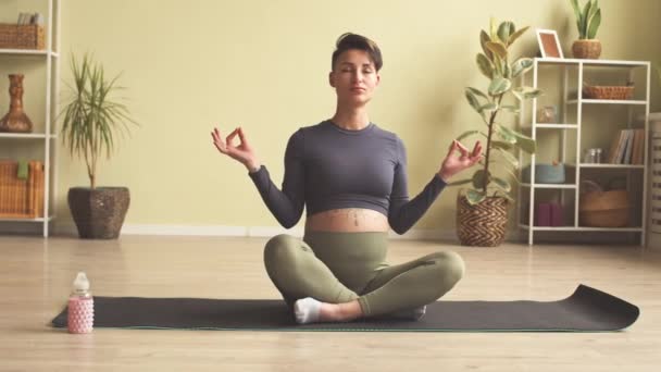 Slowmo of relaxed young pregnant woman with her hands in mudra and eyes closed meditating on floor at home - Imágenes, Vídeo