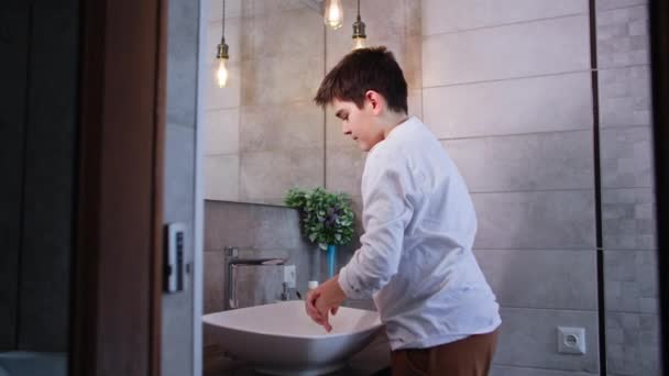reggeli higiénia, imádnivaló fiú mossa arcát vízzel, miközben áll a mosdókagyló a fürdőszobában - Felvétel, videó