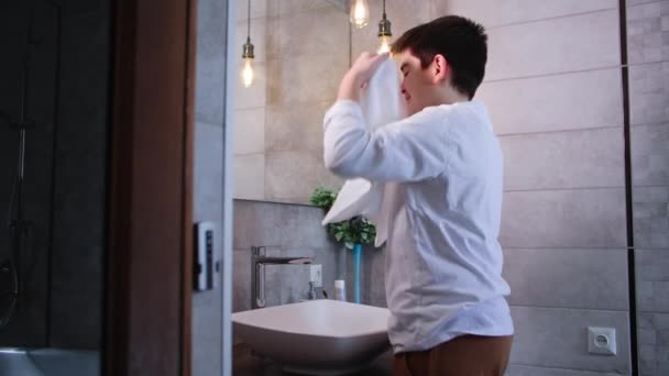 lindo niño varón haciendo rutina de la mañana cerca del lavabo, limpiando su cara con una toalla después del tratamiento de agua mirando en el espejo - Imágenes, Vídeo
