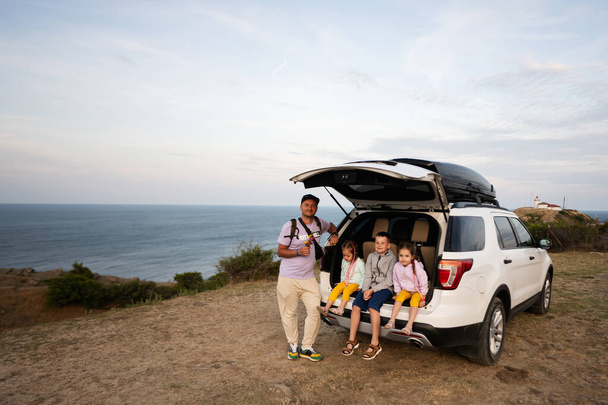 Portrait of a happy family sitting in car trunk at the beach. Cape Emine, Black sea coast, Bulgaria. - Foto, afbeelding