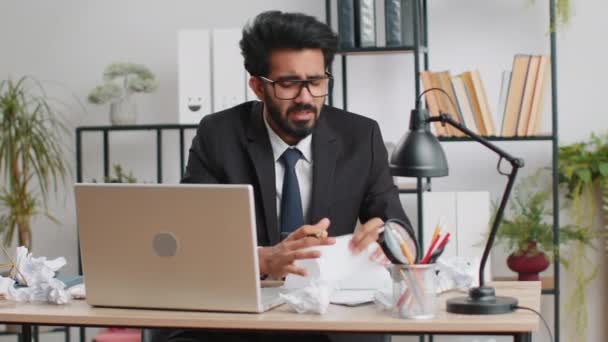 Boos woedende indiaanse man die op kantoor werkt met verkreukeld papier, zenuwinzinking op het werk, migaïne, hoofdpijn, stressbeheersing, psychische problemen, driftbuien, reactie op falen - Video