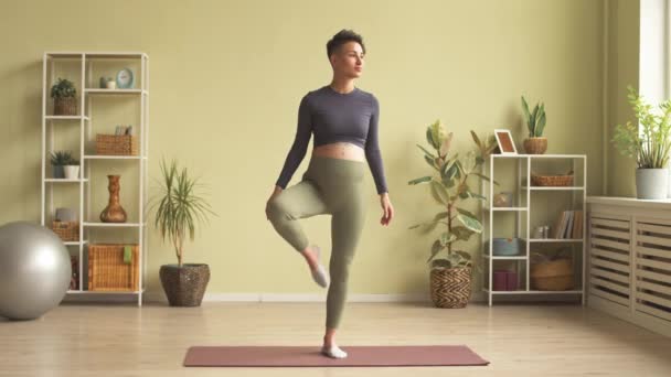 Full length shot of young slim pregnant woman standing on one leg on yoga mat indoors and meditating with her hands in mudra - Imágenes, Vídeo