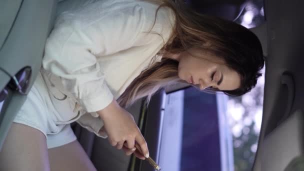 Direksiyonda oturan genç kadın sürücü akıllı telefon kullanıyor arabayı çalıştırıyor ve oradan ayrılıyor. Dikey video - Video, Çekim