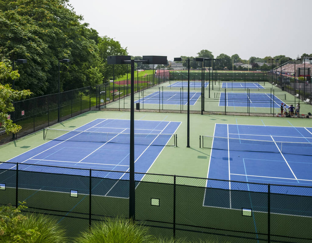 View from above of blue and green pickleball and tennis courts with lights and a b;ack fence surrounding them. - Zdjęcie, obraz