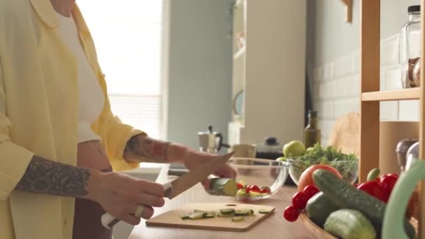 Cropped shot of tattooed pregnant woman in oversized light ye3llow shirt making healthy vegetable salad at bright modern kitchen - Filmmaterial, Video