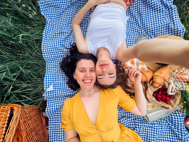 Két lány egy randin fekszik a kék takarón piknikezni a természetben. - Fotó, kép