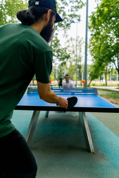 Inklusiver alter Mann spielt Tischtennis gegen einen behinderten Mann, der im Rollstuhl im Stadtpark sitzt - Foto, Bild
