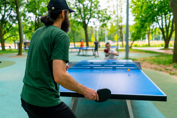 інклюзивність старий грає в пінг-понг проти чоловіка з інвалідністю, який знаходиться в інвалідному візку в міському парку - Фото, зображення