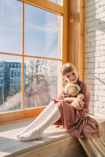 menina bonito no vestido perto da janela com urso brinquedo - Foto, Imagem
