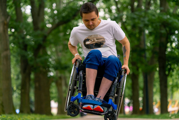 Inclusividad Un hombre con discapacidad hace acrobacias en silla de ruedas en un parque de la ciudad contra el telón de fondo de los árboles - Foto, Imagen