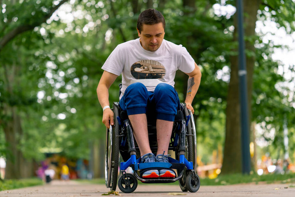 Osallisuus Vammainen mies ajaa pyörätuolilla kaupungin puiston polkua pitkin puiden taustaa vasten - Valokuva, kuva