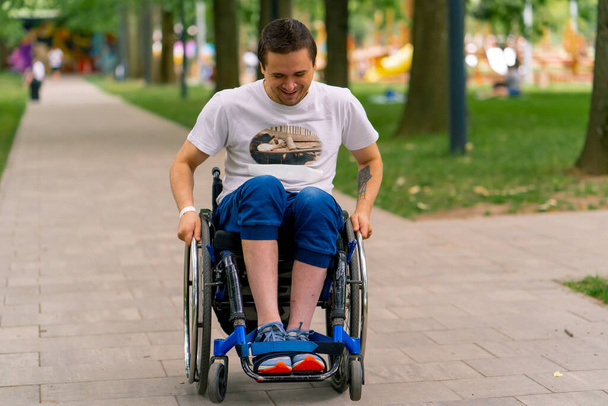 Inclusiviteit Een man met een handicap rijdt in een rolstoel langs het pad van het stadspark tegen de achtergrond van bomen - Foto, afbeelding