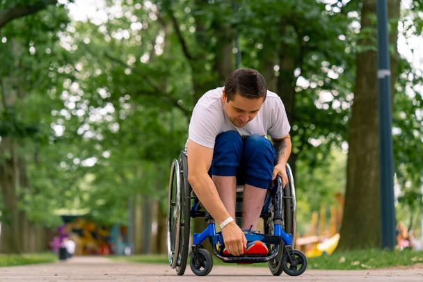 Inclusividad Un hombre con discapacidad monta una silla de ruedas a lo largo del camino del parque de la ciudad contra el fondo de los árboles - Foto, imagen