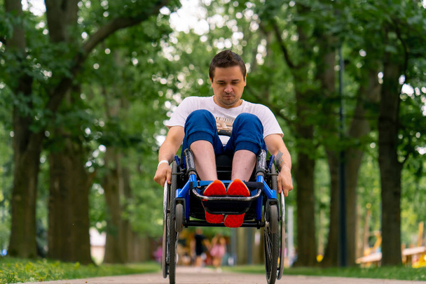 Osallisuus Vammainen mies tekee pyörätuolitemppuja puistossa puiden taustaa vasten. - Valokuva, kuva