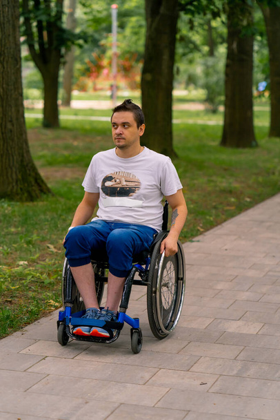 Инклюзивность Человек с ограниченными возможностями катается на инвалидной коляске по тропе городского парка на фоне деревьев - Фото, изображение
