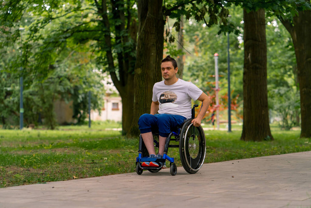 Inclusivité Un homme handicapé emprunte un fauteuil roulant le long du sentier du parc municipal sur fond d'arbres - Photo, image