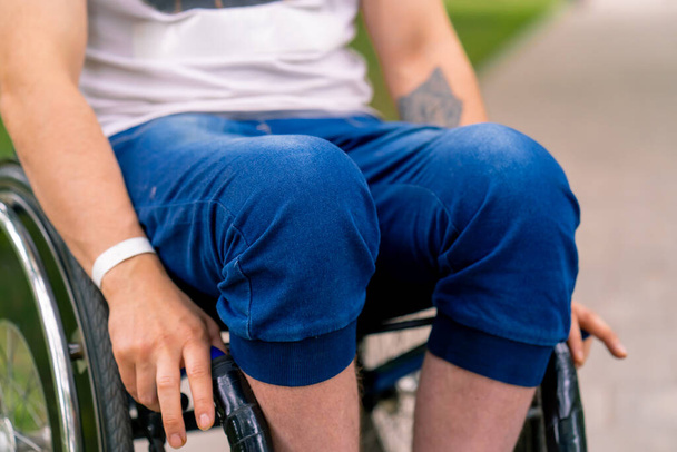 Inclusività Primo piano delle ginocchia di un uomo con disabilità che guida una sedia a rotelle nel parco cittadino - Foto, immagini