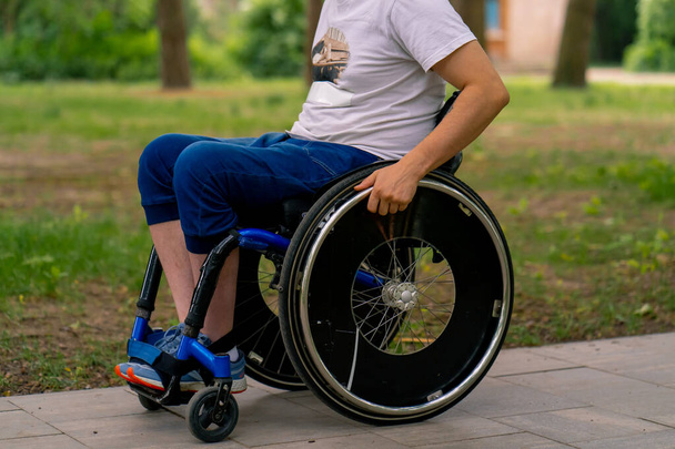 Inclusività Un giovane con disabilità cavalca su una sedia a rotelle in un parco cittadino su uno sfondo di alberi - Foto, immagini