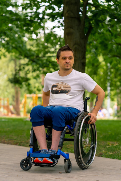 Inclusividade Retrato de um jovem com deficiência em uma cadeira de rodas em um parque da cidade contra o fundo das árvores - Foto, Imagem