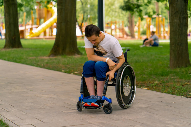 Inclusivité Portrait d'un jeune homme handicapé en fauteuil roulant dans un parc municipal sur fond d'arbres - Photo, image