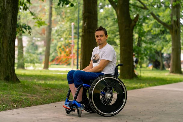 Inklusivität Porträt eines jungen Mannes mit Behinderung im Rollstuhl in einem Stadtpark vor dem Hintergrund von Bäumen - Foto, Bild