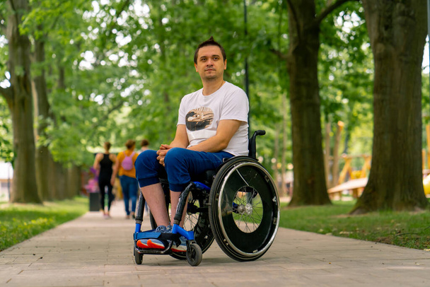 Inclusivité Portrait d'un jeune homme handicapé en fauteuil roulant dans un parc municipal sur fond d'arbres - Photo, image
