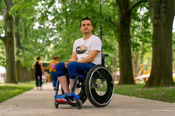 Inclusividad Retrato de un joven con discapacidad en silla de ruedas en un parque de la ciudad sobre el fondo de los árboles - Foto, imagen