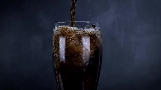 Een koel glas cola drinken met ijs, bubbels en fizz. Verse koude zoete drank gegoten over ijsblokjes. Cola glas met zomerse verfrissing op zwart. Langzame beweging - Video