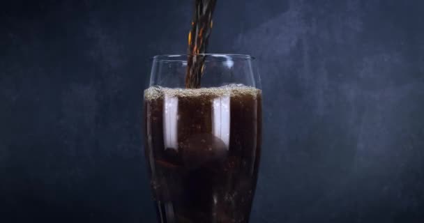 Ein kühles Glas Cola-Drink mit Eis, Blasen und Schampus. Frisches kaltes süßes Getränk über Eiswürfel gegossen. Cola-Glas mit sommerlicher Erfrischung auf schwarz. Schneller Vorlauf 4k - Filmmaterial, Video
