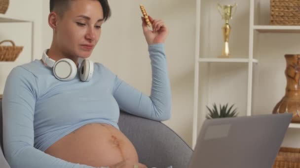 Young Caucasian pregnant woman eating sweet biscuit waffles while working on laptop from home - Footage, Video