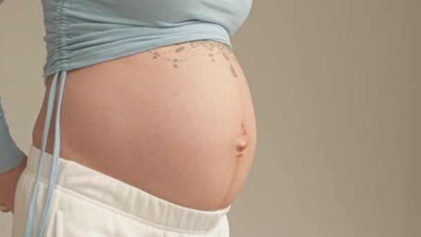 Midsection of pregnant woman measuring her tattooed bare belly at home - Materiał filmowy, wideo