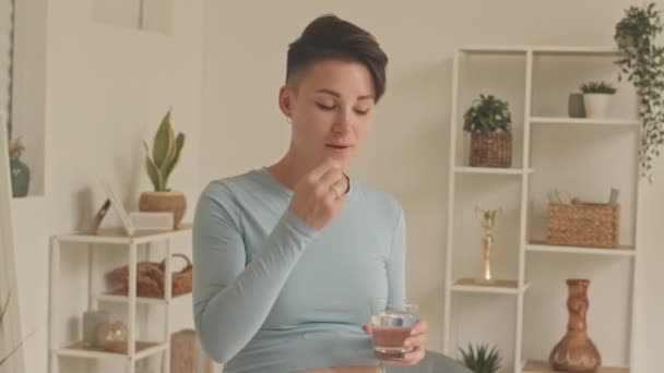 Medium shot of modern young short haired pregnant woman taking prenatal supplements at home - Filmagem, Vídeo