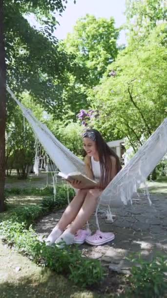  beautiful hippie girl is sitting in a hammock on a summer day, reading a book. High quality 4k footage - Filmati, video