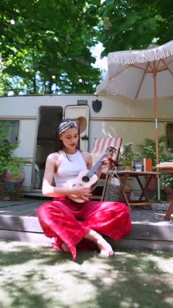  beautiful hippie girl is singing a song and playing the guitar near the trailer. High quality 4k footage - Πλάνα, βίντεο